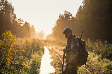 Bird Hunter at Sunrise going for hunt in a forest with his shotgun rifle.