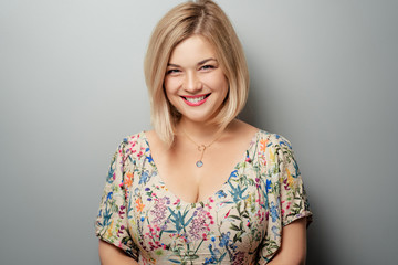 Portrait of happy blonde woman smiling and looking at camera on grey background.