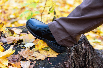 Human foot in shoes and brown pants against the background of autumn fallen leaves.