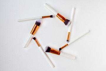 Flat lay top view of female cosmetics brushes set for makeup on white background. Cosmetics and beauty concept with space for text in the middle.