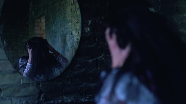 Insane woman holding head and convulsing near mirror, possessed by evil demon