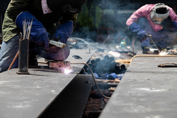 Worker using electric wheel grinding on steel structure in factory.