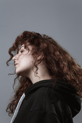 Portrait of a beautiful curly-haired girl with redheads on a gray background