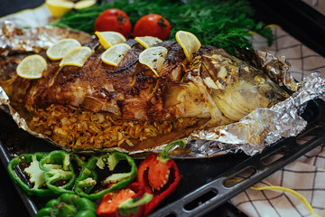 Baked fish river carp with aromatic herbs, spices, salt, vegetables, lemon, garlic, top view, healthy food, diet or cooking concept.