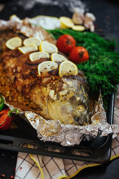 Baked fish river carp with aromatic herbs, spices, salt, vegetables, lemon, garlic, top view, healthy food, diet or cooking concept.