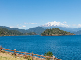 The amazing Choshuenco Volcano surrounded by clouds, over the waters of Lake Panguipulli, in southern Chile. - 296435140