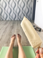 мA woman with bare feet holds in her hands a delicious white ice cream on a stick sitting on the floor