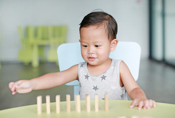 Portrait of little baby boy playing wood blocks tower game for Brain and Physical development skill in a classroom. Focus at children face. Child learning and mental skills concept.