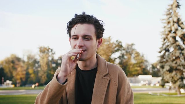 Portrait of handsome stylish young smoking smoking marijuana joint in park, slow motion