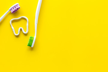 Teeth brushing concept. Tooth drawn with toothpaste near toothbrushes on yellow background top view...