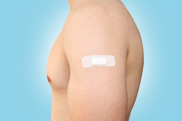 young sports man with a naked torso with a medical plaster on his shoulder, concept of vaccination, injection, close-up