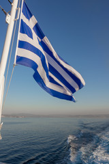 Greek flag flying in the wind over ocean behind boat
