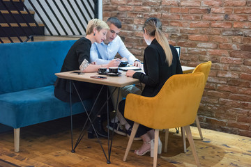 Fototapeta premium Multiracial business people working connected with technological devices at the bar. Group of three young creative coworkers working with new startup project.