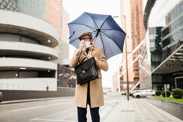 Stylish businessman with an umbrella leaves the office because of a cold