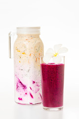 Jug of sweet colorful layered yougurt with fruits and berries and a glass of dragon fruit juice decorated with flower isolated at white background. Concept of detox and vegan healthy lifestyle.