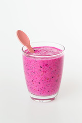 Closeup glass of berries purple smoothie with plastic spoon at white background with copyspace. Concept of healthy vegan lifestyle and super food. Vertical orientation.