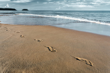 Texture sand and footprints near the water on the beach.The waves breaking the footprints on the beach.