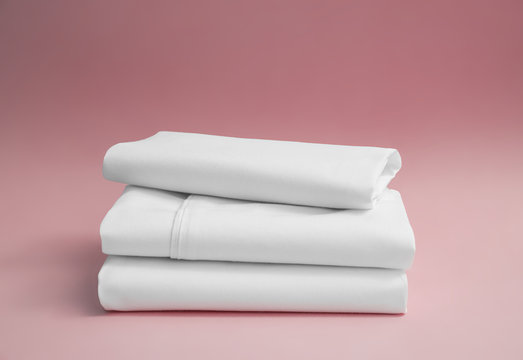 Stack of white bedding against pink backdrop, folded soft bed clothes, stack of white cotton sheets on a pink background for advertising, commercial and mock up