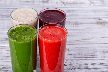 Fresh avocado, strawberry, blueberry and banana smoothie on white wooden table. Healthy cocktails with fresh fruits. Closeup four drinks, copy space