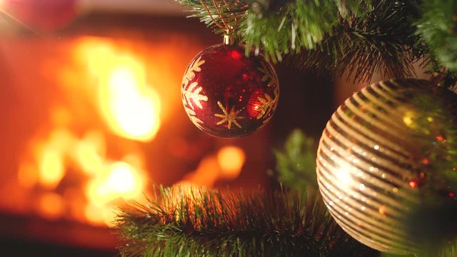 Closeup 4k video of red and golden baubles hanging on Christmas tree against burning fire in firepalce at house. Beautiful backdrop for winter holidays