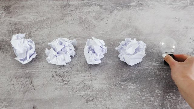 creative block concept, scrunched paper sheets and hand placing lightbulb next to them