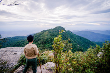 Trekker sitting on the mountain with Beautiful Sunrise and sea of mist in the morning on Khao Luang mountain in Ramkhamhaeng National Park,Sukhothai province Thailand