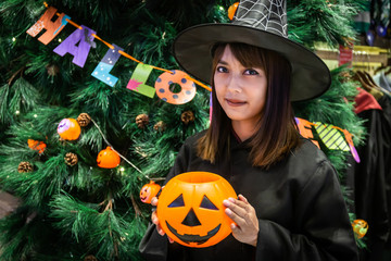 Fototapeta premium Beautiful young surprised woman or Halloween Witch dark style with holding a pumpkin in Halloween celebrate night party. Copy space background and soft or select focus