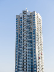 A new high-rise residential building rises in the clear sky. Light tall and narrow facade