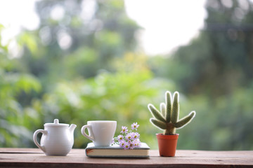 white cup with teapot and small cactus with purple daisy flower and book on wooden table