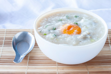 Rice porridge or congee with egg in white bowl and spoon on wooden table.