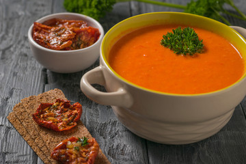 Cream of pepper soup with herbs and toast on a wooden table.