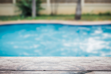 Wooden top table foreground with the blur blue swimming pool in background.