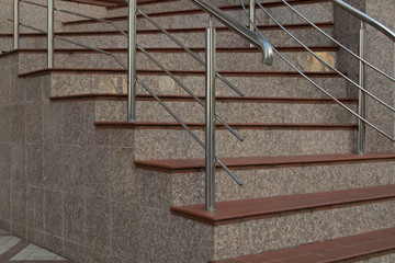 Horizontal steps made of brown ceramic tiles turning stairs made of gray marble tiles with chrome...