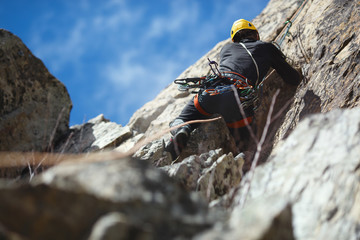 Climber climbs a stone wall against a blue sky, close-up, back view. Climbing gear. Climbing equipment.