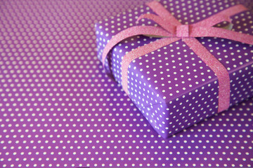 Violet gift with pink ribbon on the violet polka dot background