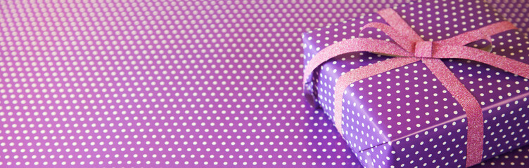 Obraz premium Violet gift with pink ribbon on the violet polka dot background