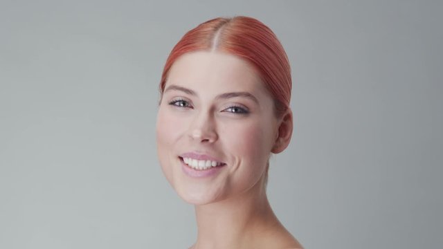 Studio portrait of young, beautiful and natural redhead woman applying skin care cream. Face lifting, cosmetics and make-up.