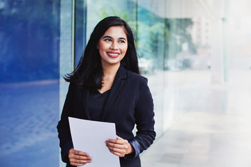 Young successful indonesian woman holding documents while standing outside the office building