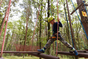 Little boy in helmet spend his leisure time in adventure playground.