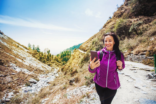 Beautiful sporty woman using her phone while trekking outdoors in Dharamsala, India