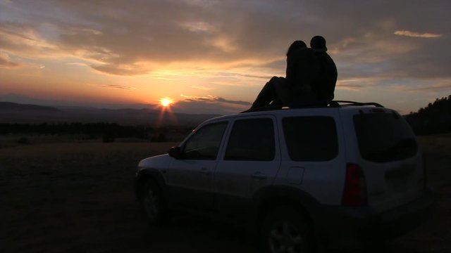 A Silhouette of a Couple sitting on top of a SUV at Sunset.