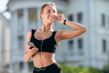 Happy girl in  black sportswear with earphones holding a smartphone.- Image