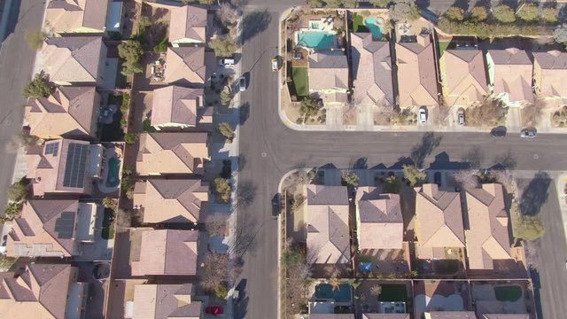 AERIAL TOP DOWN: Flying over terraced houses in a luxury suburban neighborhood in Nevada. Cinematic shot of row houses and backyards in the sunny suburbs of Las Vegas. Empty roads run through suburbia