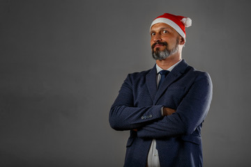 Bearded man in a blue jacket and a Christmas hat on a gray backround