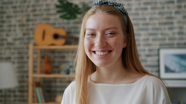 Close-up slow motion portrait of joyful girl smiling laughing looking at camera indoors in modern loft style apartment. Happy young people and house concept.