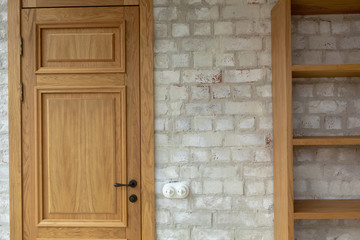 Closed oak panel door with black door knob beside empty bookcase against white brick wall with...