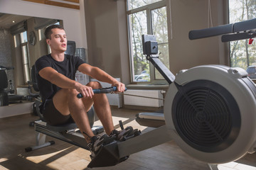The athlete is engaged in the gym, the Young man works on the rowing simulator