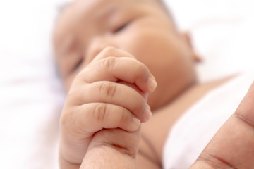 Newborn baby holding father's finger While sleeping comfortably on the white mattress During bedtime, the child's brain will work. To enhance Memory-boosting and learning-building skills