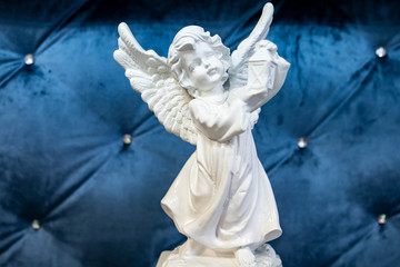Beautiful statue of an angel child holding a lamp in hands. Small statue of a baby angel on a soft blue background