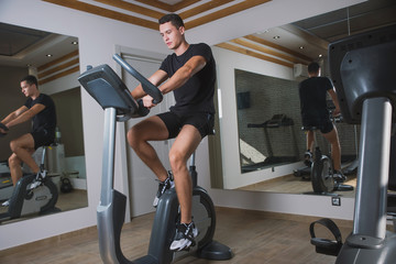 An athlete is engaged in the gym, a Young man does cardio on an exercise bike